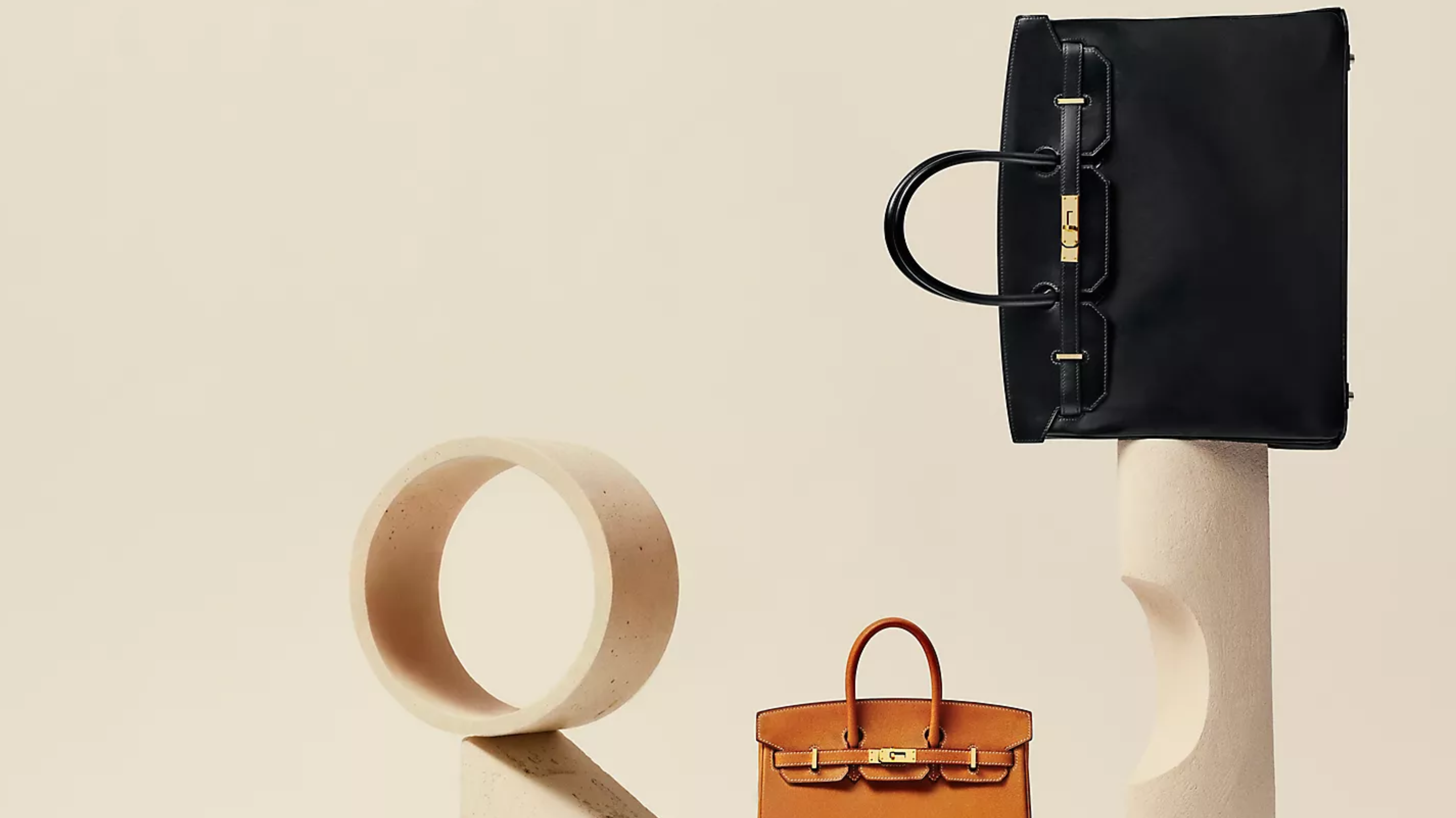 Hermès Birkin and Haut à Courroies handbags displayed in a minimalist studio setting.
