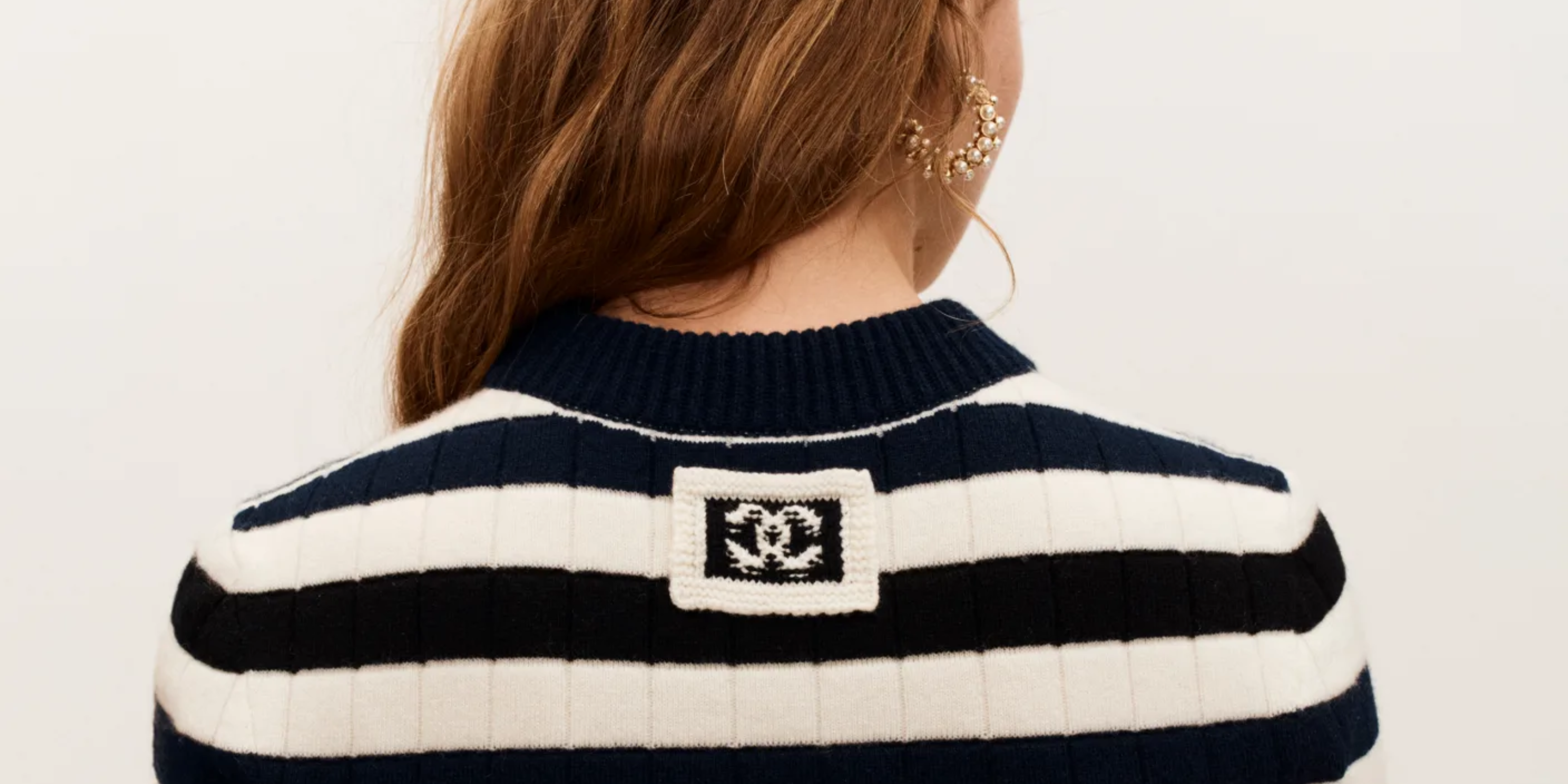 photo qui vient du site chanel, dos d'une femme qui a un pull rayé blanc et noir avec le logo chanel en assez gros 