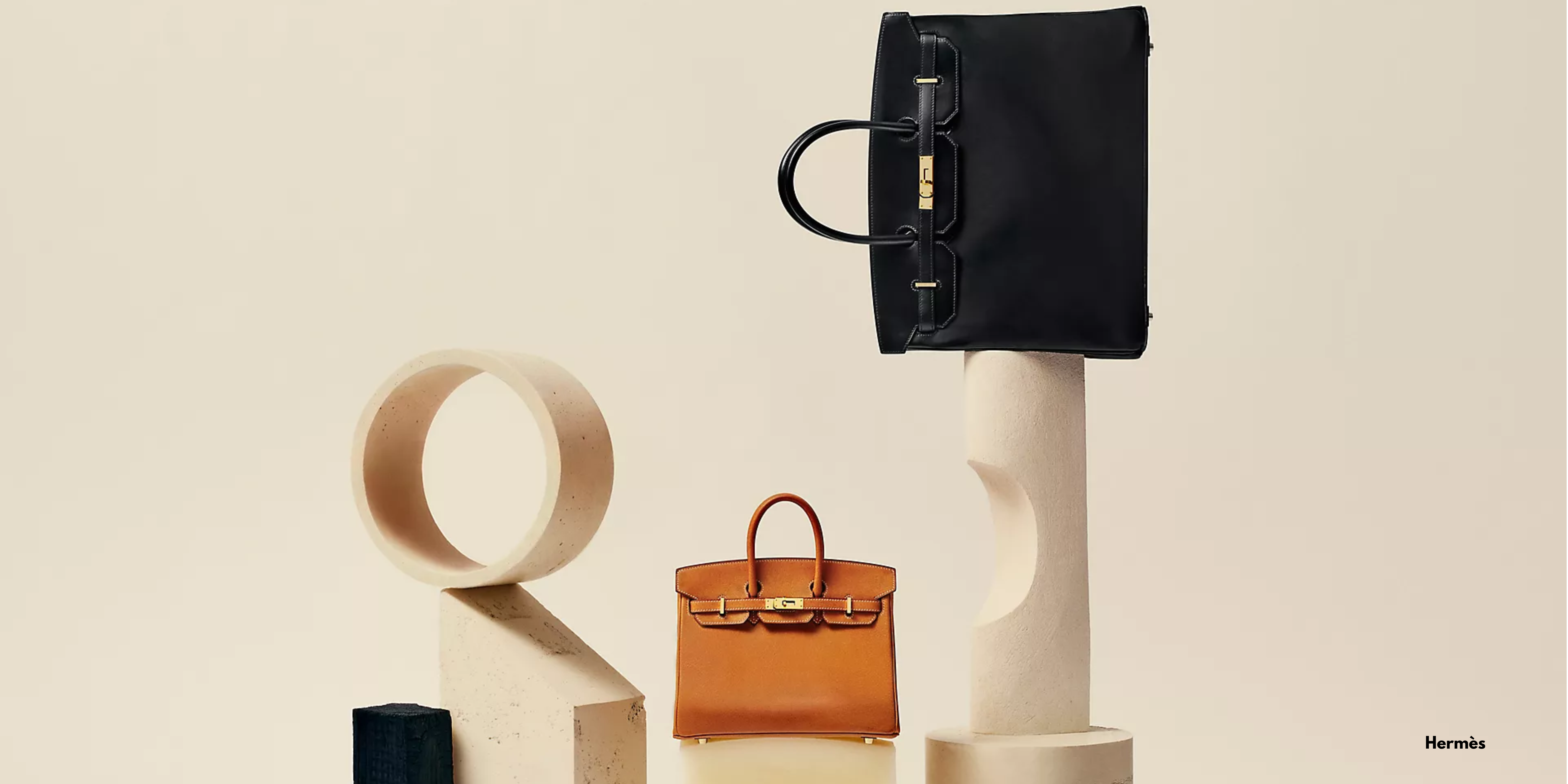 Hermès Birkin and Haut à Courroies handbags displayed in a minimalist studio setting.
